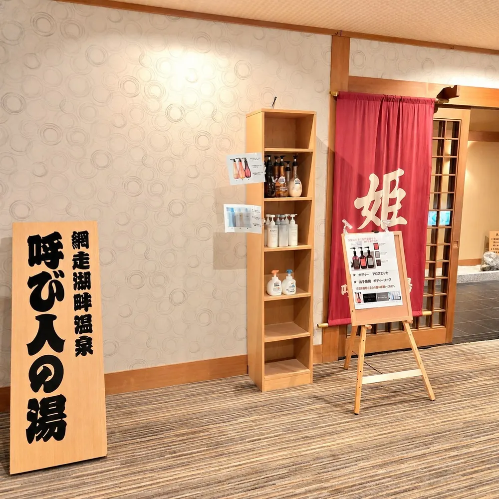 「呼び人の湯」の看板と、「姫」の暖簾がかかる女性用の入口、シャンプー類の棚